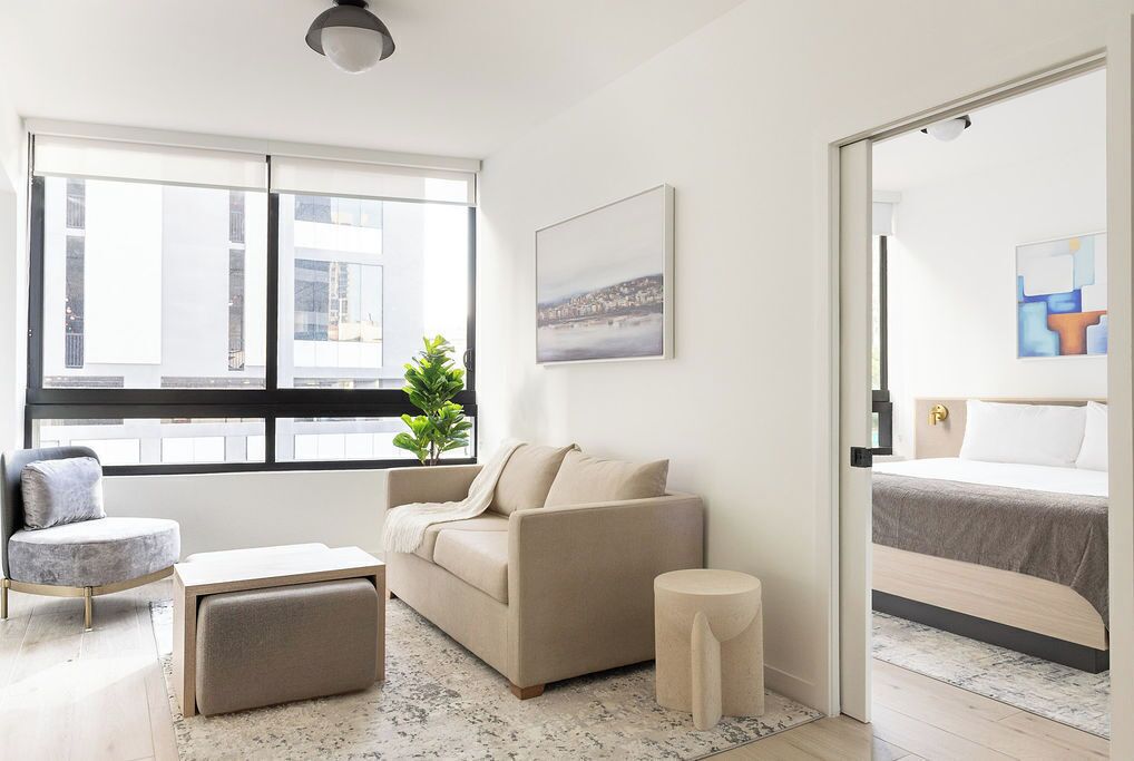 Habitación de hotel moderna con un ventanal grande, un sofá, una mesita redonda y una cama.