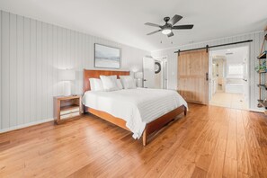 A bedroom with a wooden bed, a nightstand, a ceiling fan, and a sliding door leading to a bathroom. - Seven Devils Sky Haven: Hot Tub, Tubing, and Mountain Views (Seven Devils)