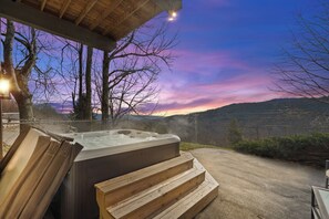 Uma banheira de hidromassagem com degraus de madeira, um banco e vista para uma paisagem montanhosa ao pôr do sol.