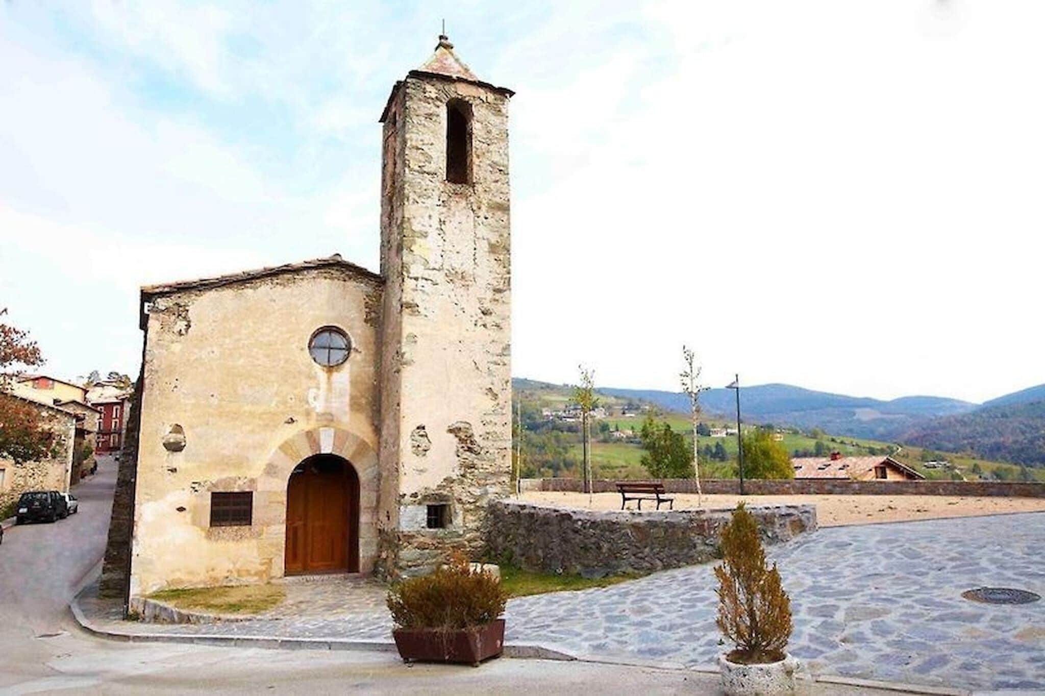 Une petite église en pierre dotée d’un clocher, d’une cour pavée et d’un banc.