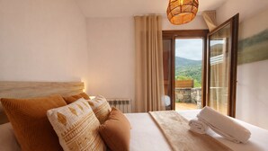 A hotel room with a large bed, a view of the outdoors, and a window with curtains. - Vall de Muntanyes - Costabona (Molló)