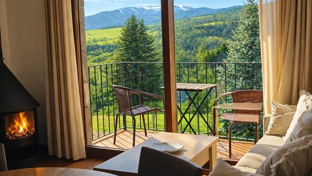 Un balcon offrant une vue sur un paysage montagneux, aménagé avec des fauteuils et une table en osier.
