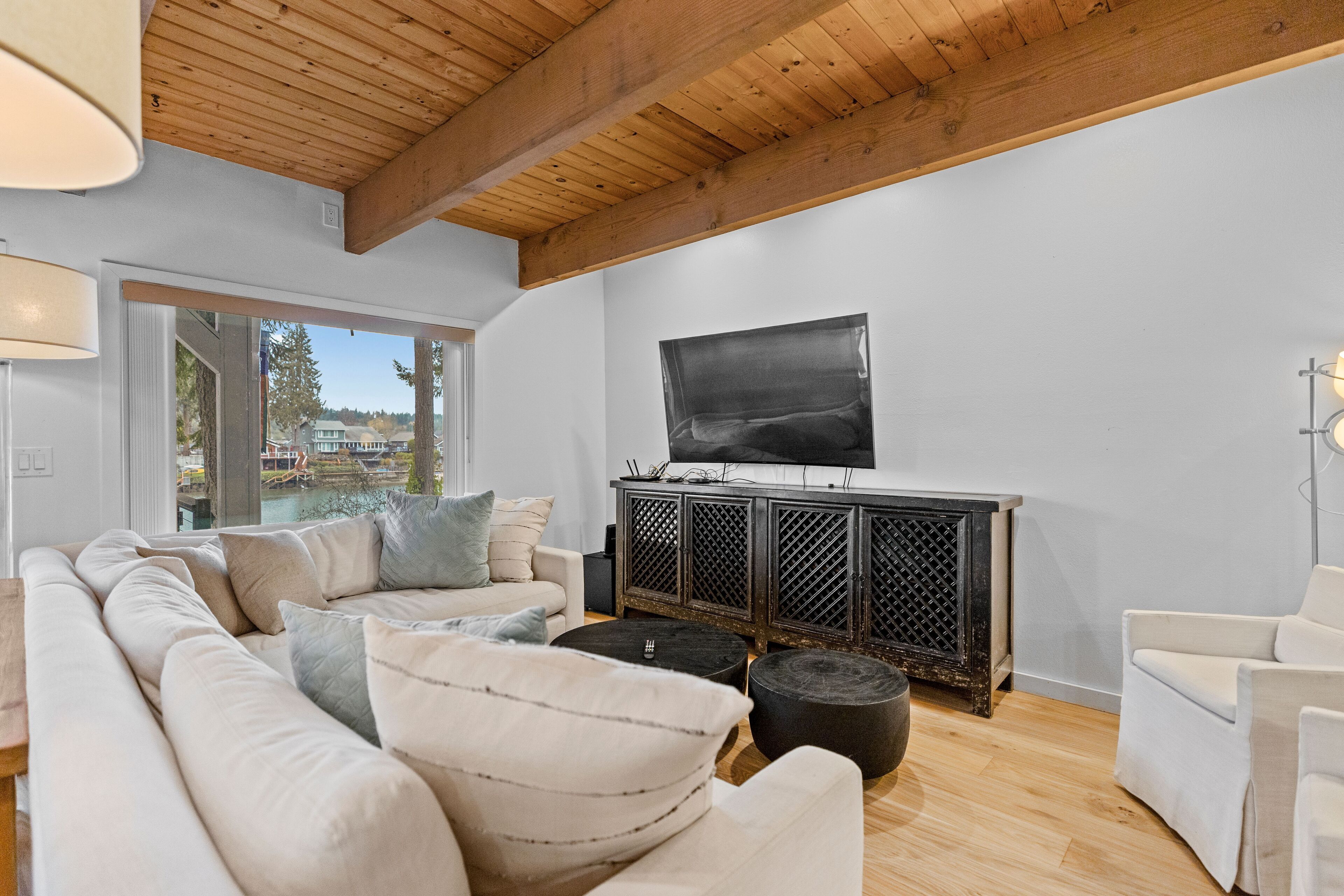 Una sala de estar moderna con un sofá grande, un televisor sobre un mueble negro y vistas al exterior.