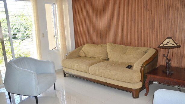 Un salón con sofá color beige, un sillón azul claro y una mesita de madera con lámpara.