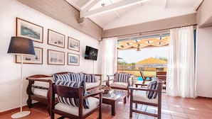 A room with wooden furniture, a TV, framed pictures, and a view of a pool and outdoor area. - Barbati Beach - Villa Lefkada (Barbati)