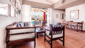 A room with a bed, a sofa, a dining table, and chairs. There is a window with curtains, a ceiling fan, and a view of the outside. - Barbati Beach - Villa Lefkada (Barbati)