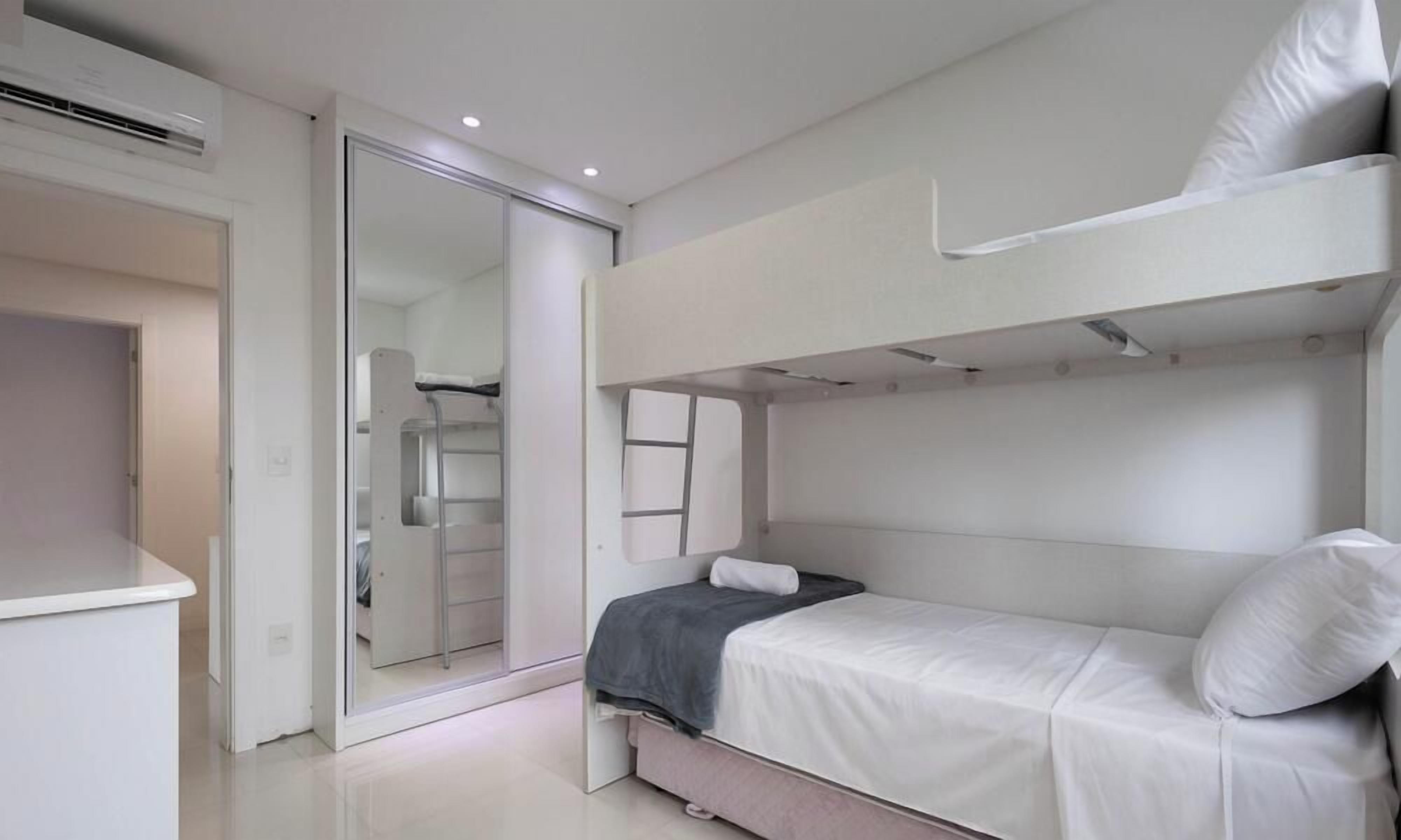 Une chambre avec un lit superposé, un placard à porte coulissante, un bureau blanc et un lit avec un oreiller.