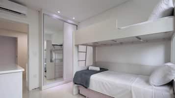 Een slaapkamer met een stapelbed, een inloopkast met schuifdeuren, een wit bureau en een bed met een kussen.