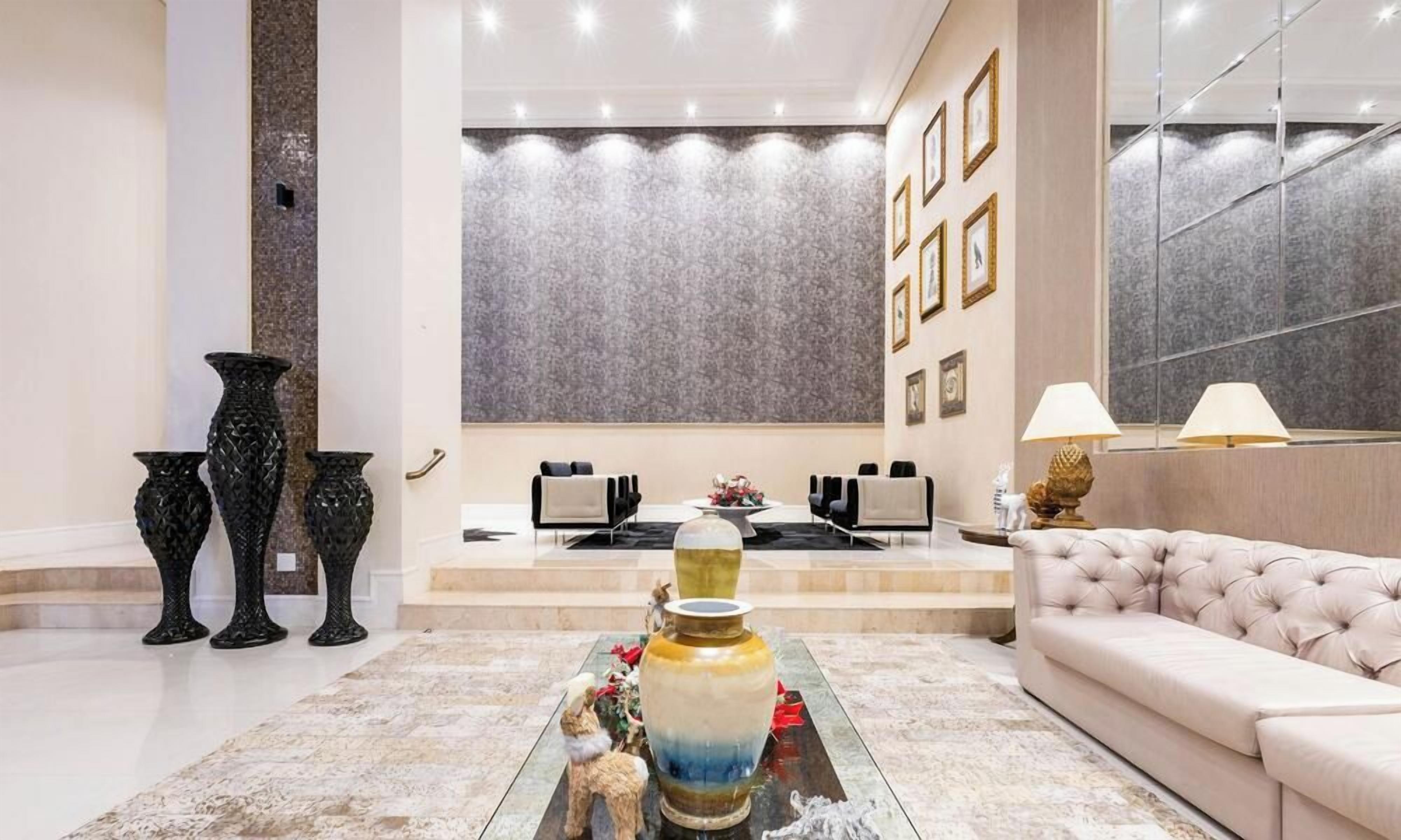 Een moderne lobby met een zithoek, een grote bloemenvaas als middelpunt en een wand met ingelijste foto's.