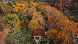 Uma casa rodeada por folhagem outonal, com montanhas ao fundo e uma estrada de terra que leva até ela.