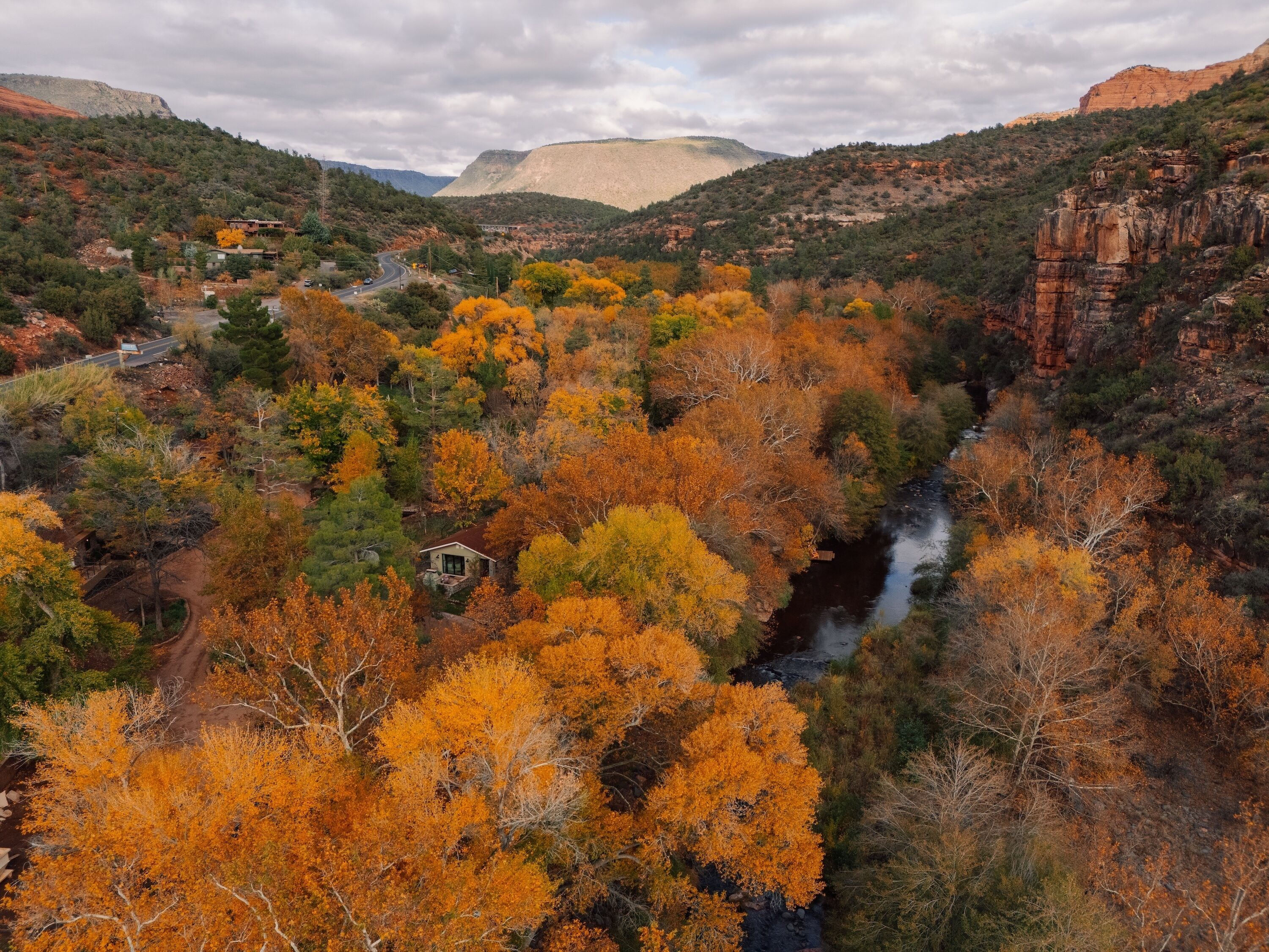 A canyon with autumn foliage, a river, and a small cabin.