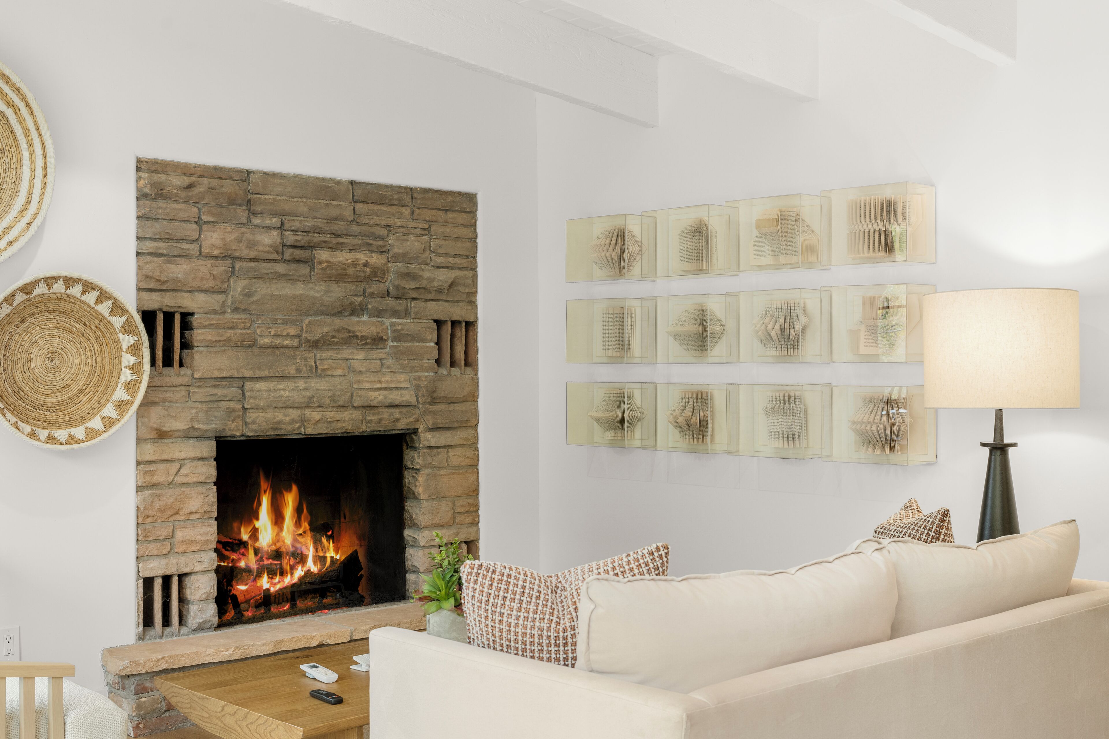 Ein Wohnzimmer mit Kamin aus Stein, einem beigen Sofa und Wandbildern.