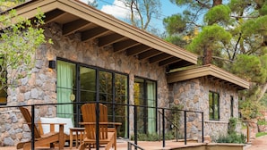 Uma casa de pedra com um pátio, deck de madeira e área de estar ao ar livre.