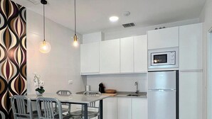 A modern kitchen with white cabinets, a stainless steel refrigerator, a microwave, and a dining area with a table and chairs. - Apartamentos Realejo Campo Príncipe 3000 (Granada)