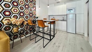 A modern kitchen with white cabinets, a built-in oven, and a microwave. There is a dining area with a table and chairs, and a decorative wall with a geometric pattern. - Apartamentos Realejo Campo Príncipe 3000 (Granada)
