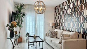 A modern living room with a sofa, a glass coffee table, a chandelier, and a patterned wall. - Apartamentos Realejo Campo Príncipe 3000 (Granada)