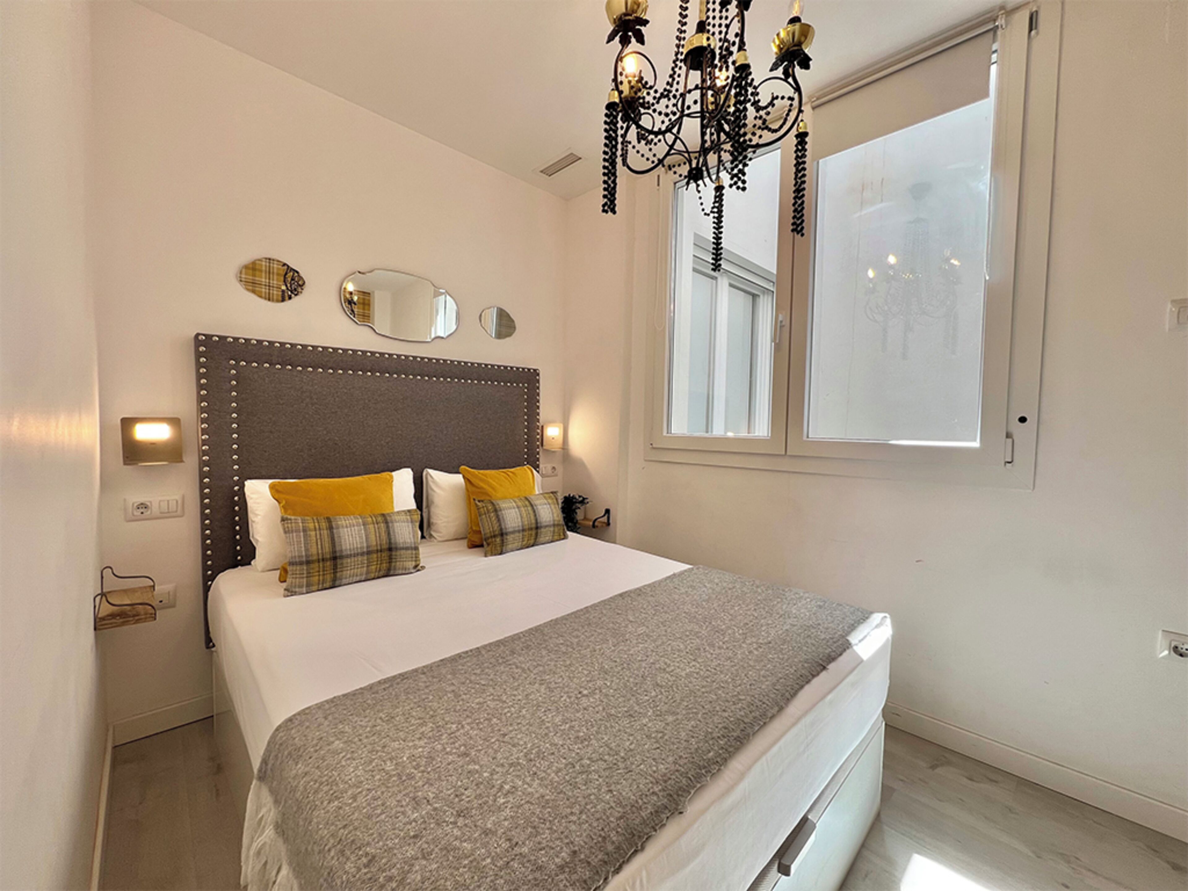 A bedroom with a large bed, a chandelier, a window, and a mirror on the wall.