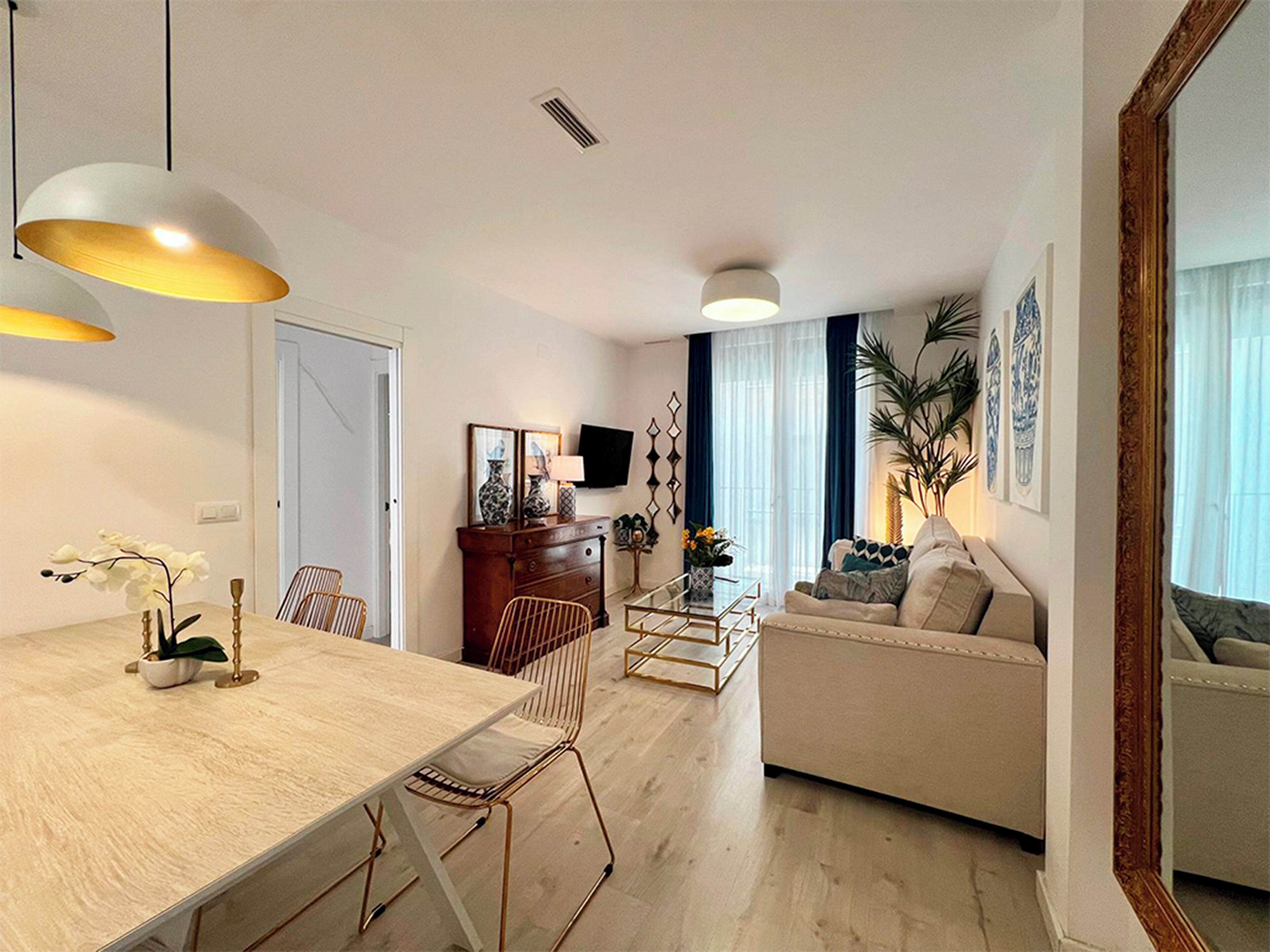 Ein modernes Wohnzimmer mit Essbereich, ausgestattet mit einem Holztisch, Stühlen, einer Couch und einem an der Wand befestigten Fernseher.