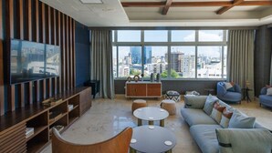 Ein modernes Wohnzimmer mit einem großen Fernseher, einem Sofa, zwei runden Tischen und Blick auf die Stadt durch große Fenster.