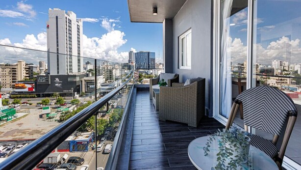 Ein Balkon mit Blick auf eine Stadtlandschaft, mit Korbmöbeln und einer Glasdoor, die zu einem Außenbereich führt.