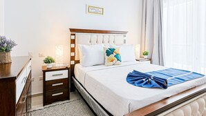 A neatly arranged bedroom with a bed, bedside tables, a nightstand, and a wall-mounted sign. - Spacious and Elegant 2BR Condo, King size Bed, Full AC, Pool, Steps to Hard Rock (Punta Cana)