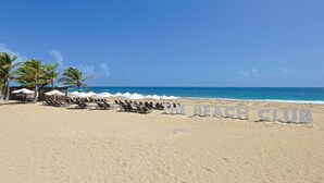 A beach with sun loungers and umbrellas, and a sign that reads "THE BEACH CLUB". - Spacious and Elegant 2BR Condo, King size Bed, Full AC, Pool, Steps to Hard Rock (Punta Cana)