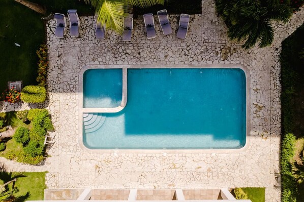 An aerial view of a rectangular swimming pool with a stone border, surrounded by a stone patio.