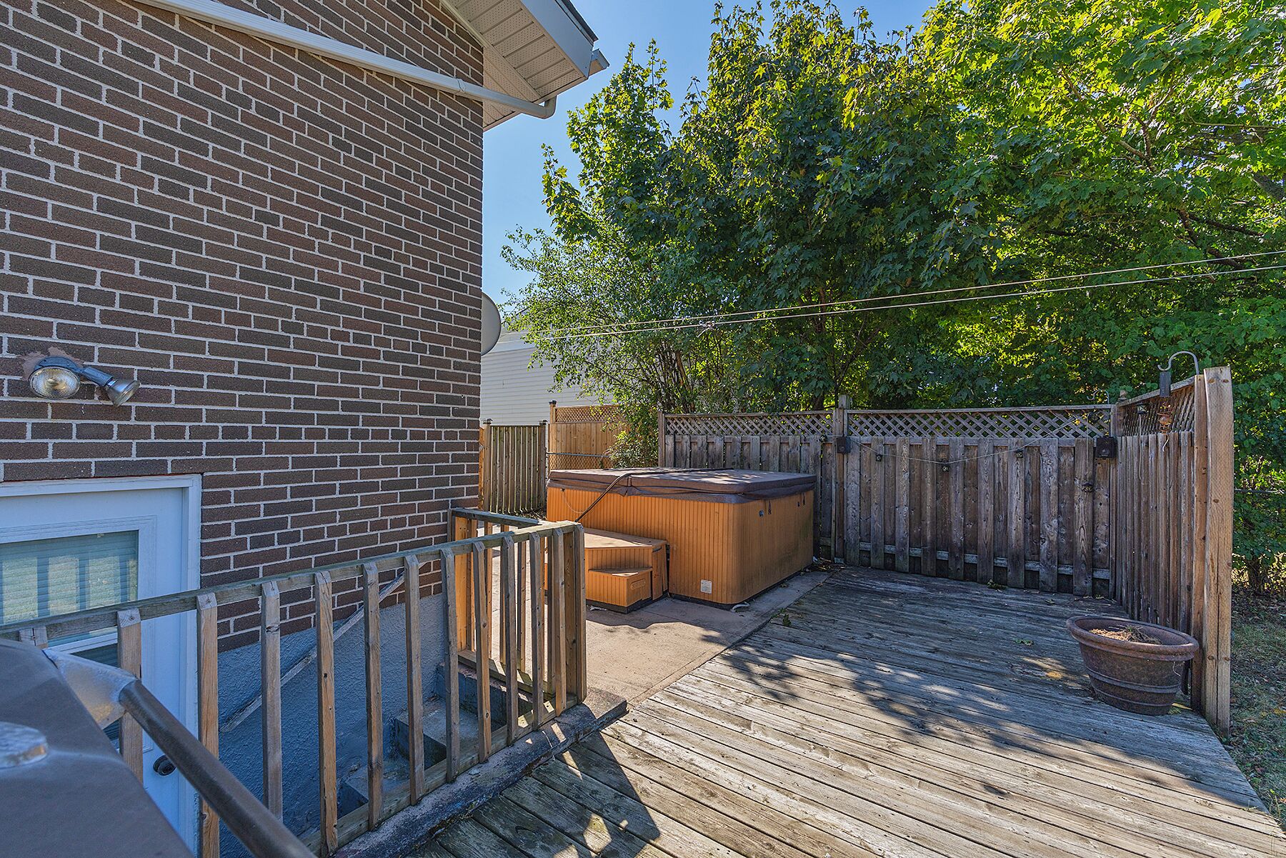 A wooden deck with a hot tub, a brick wall, and a wooden fence.