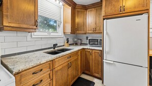 Cucina con mobili in legno, frigorifero bianco, forno a microonde e una finestra con persiane.