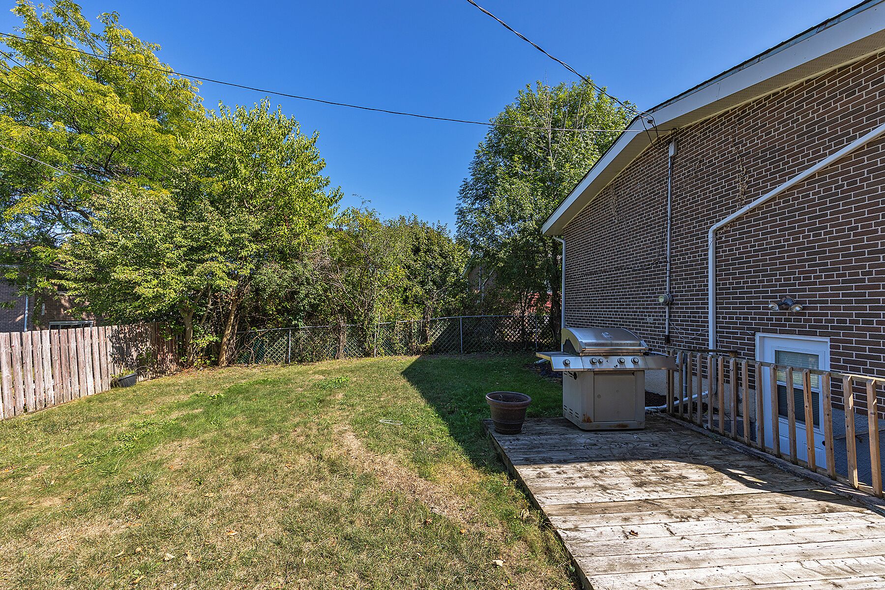 Un jardin avec un bâtiment en briques, une terrasse en bois et un barbecue.