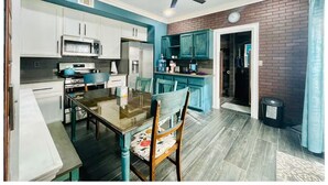 Una cocina compacta con armarios blancos, un microondas, estufa y sillas color turquesa alrededor de una mesa de vidrio.