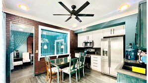 Una cocina moderna con comedor, que incluye un ventilador de techo, gabinetes blancos, un refrigerador y una mesa de comedor con sillas.
