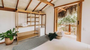 Una stanza con soffitto in legno, un letto con copriletto decorato, un mobiletto a scaffali in legno e una pianta in vaso.