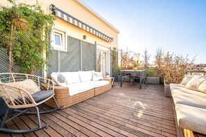 Eine Holzterrasse mit einer Couch, einem Esstisch und Stühlen.