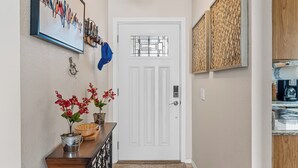 Un pasillo con una puerta blanca, una obra de arte enmarcada, una planta en maceta y un mueble de madera.