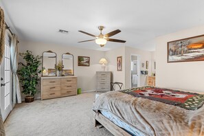 A bedroom with a bed, a dresser, a nightstand, a ceiling fan, and a painting on the wall. - Private Pool, Home Away From Home! (Bullhead City)