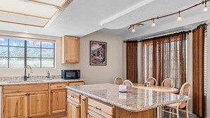 Una cocina con armarios de madera, encimera de granito, una mesa de comedor con sillas, un microondas y una ventana con cortinas.