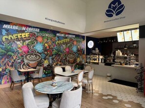 A coffee shop interior with a colorful mural, seating area, and a counter with a menu display. - Spacious Modern Studio • Pool & Balcony • Circ Hotel (Hollywood)