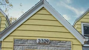 Ein Haus mit einer Stein-Fassade, einer weißen Haustür und der Hausnummer 2329 darüber.