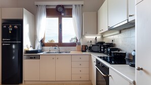 Eine moderne Küche mit einem schwarzen Kühlschrank, einer Mikrowelle, einem Herd und einem Geschirrspüler. Ein Fenster mit Vorhängen und eine Uhr an der Wand sind ebenfalls vorhanden.