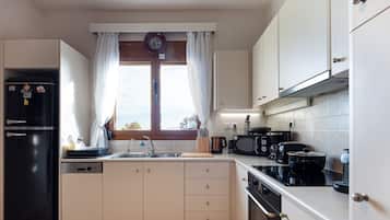 Uma cozinha moderna com geladeira preta, micro-ondas, fogão e lava-louças. Há uma janela com cortinas e um relógio na parede.