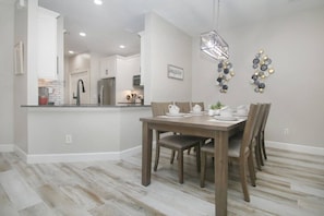 A dining area with a wooden table and chairs, a kitchen in the background, and a decorative wall piece. - Gated 3BR 2.5BA Home Near Disney (Kissimmee)