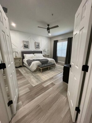 A bedroom with a bed, bedside tables, a bench, a ceiling fan, and a window with curtains. - Gated 3BR 2.5BA Home Near Disney (Kissimmee)
