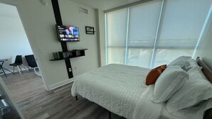 Ein modernes Hotelzimmer mit einem großen Bett, einem an der Wand befestigten Fernseher und Blick ins Freie durch große Fenster.