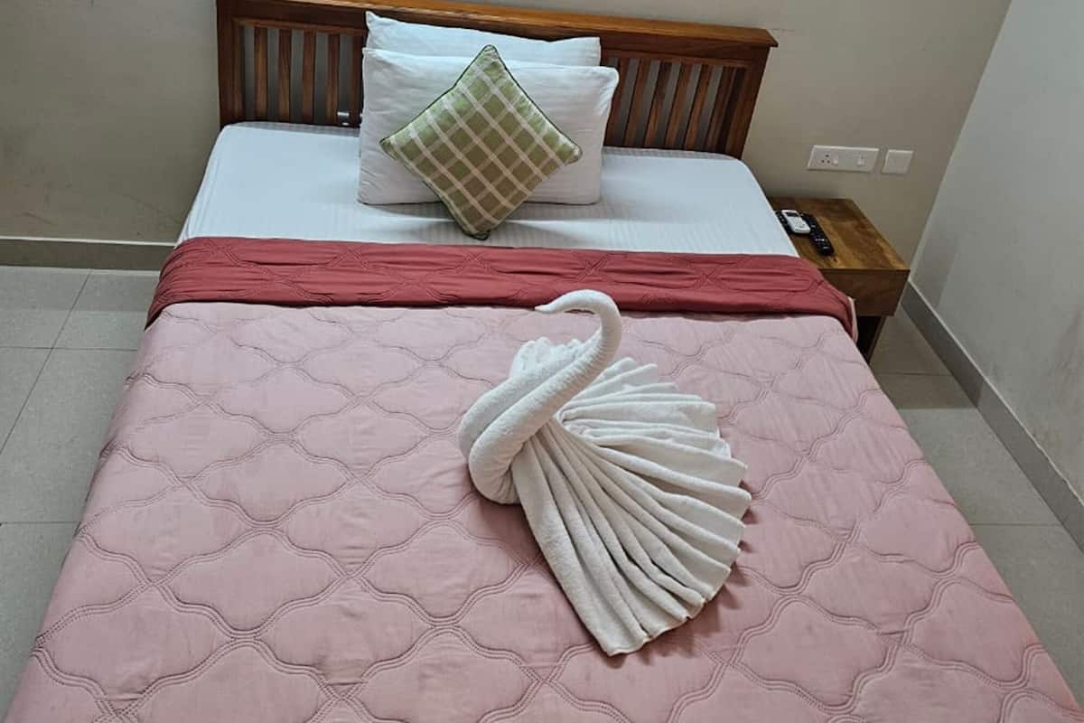 A neatly made bed with a pink quilt, a wooden headboard, a green and white pillow, and a white towel arranged in a swan shape on the bed.