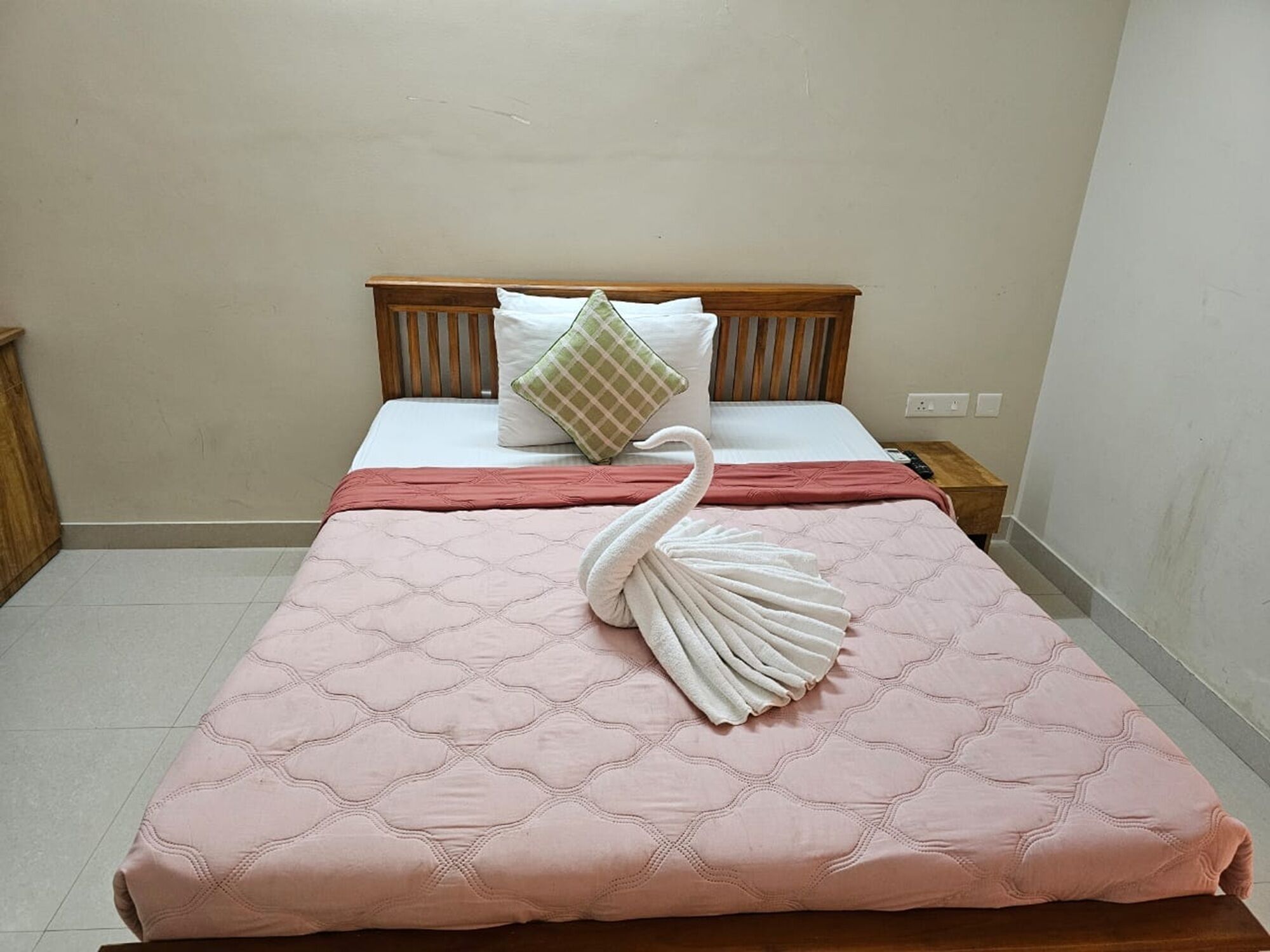 Een net opgemaakt bed met een roze deken, een houten hoofdbord en een handdoek in de vorm van een zwaan op het bed.