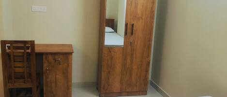 A bedroom with a wooden wardrobe, a desk, and a bed.