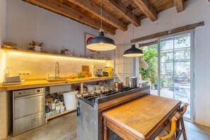 A kitchen with wooden beams, a large island, stainless steel appliances, and a view through a glass door.