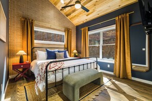 Une chambre à coucher avec un lit, des tables de chevet, un banc et de grandes fenêtres avec des rideaux.