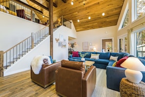 Un vaste salon avec un escalier, un ensemble de canapés bleus et un plafond en bois.